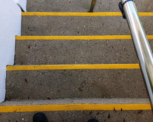 Yellow high visibility textured paint nosings applied to an existing concrete stairway